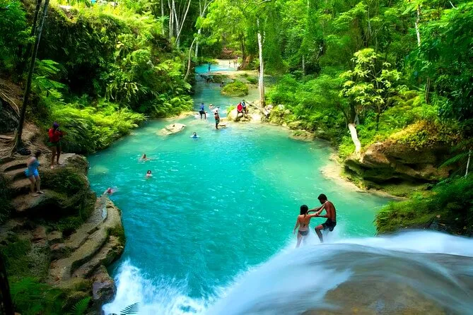 Swimmers jumping from limestone rocks into the turquoise Blue Hole pool on an Ocho Rios excursion in Jamaica